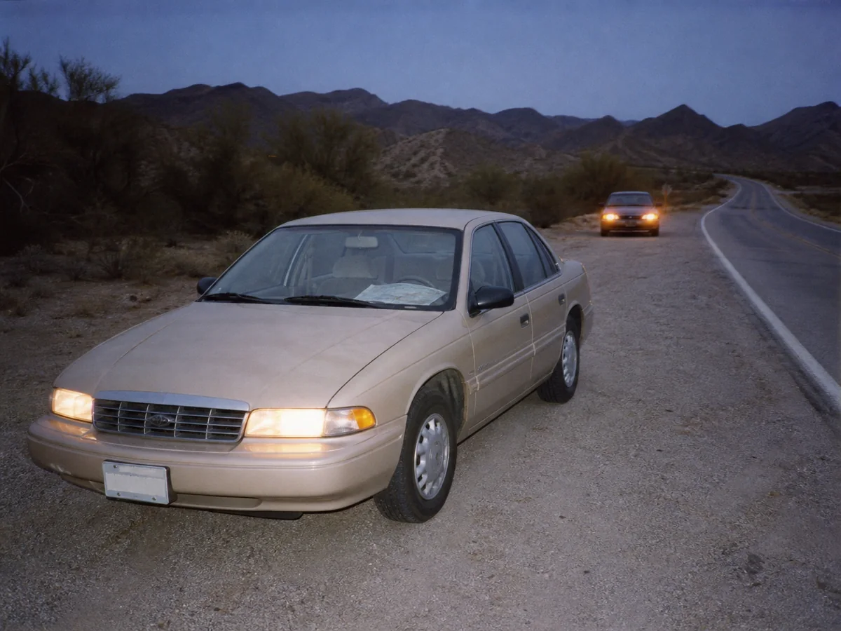 Beige sedan at a gravel turnout with a paper map visible through the windshield