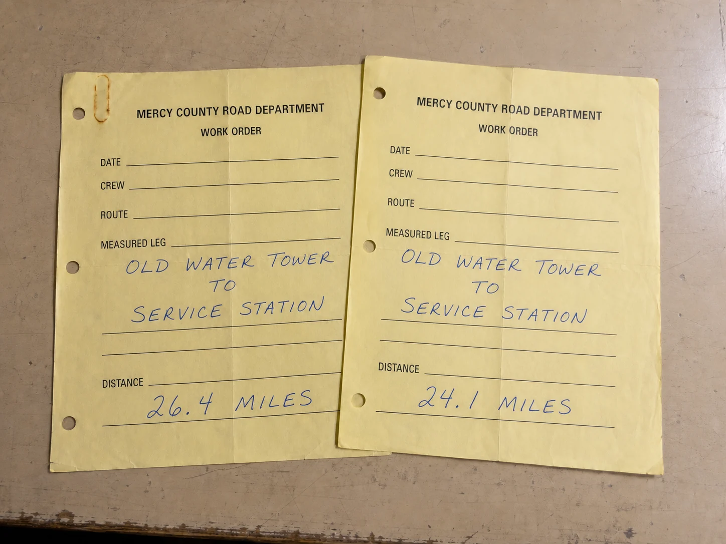 Two yellow Mercy County Road Department work orders with different distances for the same measured leg